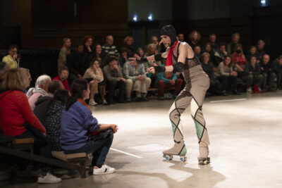 le danseur debout en rollers, les pieds écartés en position d'arrêt, interagit avec le public assis à gauche de l'image - Agrandir l'image 6 sur 14, fenêtre modale