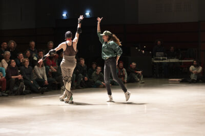 De dos, le danseur à rollers est flanqué à sa droite d'une jeune femme en tenue de style sport, bomber et casuqette kaki brillant; tous deux lèvent un bras en l'air en un geste qui évoque le flamenco - Agrandir l'image 8 sur 14, fenêtre modale