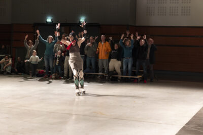 Tout sourire, depuis les gradins en fond de scène, le public participe au spectacle en imitant le geste du danseur au premier plan, mains en l'air - Agrandir l'image 9 sur 14, fenêtre modale
