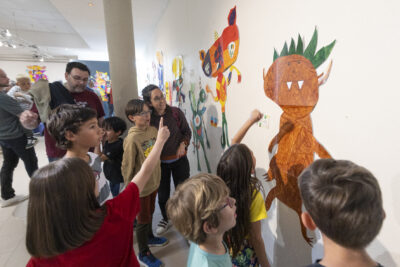 La mine ébahie, des enfants sont absorbés par l'étude des motifs de monstres affichés autour d'eux en salle d'exposition - Agrandir l'image 11 sur 13, fenêtre modale