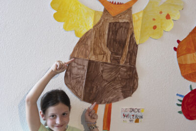 plan rapporché sur une fillette en jean et tee-shirt debout sourire timide elle pose devant l'effigie d'un grand monstre mi-fillette mi-personnage imaginaire, à ailes et tête jaune sympathique au-dessus de sa tête - Agrandir l'image 12 sur 13, fenêtre modale