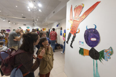 Regard interrogateur d'un jeune garçon qui scrute deux monstres volants adhésivés sur un pan de mur blanc d'exposition - Agrandir l'image 13 sur 13, fenêtre modale