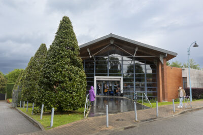 De dos, une comédienne en parka violette se tient devant un groupe de quatre musiciens classiques en train de jouer devant l'entrée de la Médiathèque de Tournefeuille. Deux sont assis et jouent de la guitare tandis que les autre deux autres jouent des instruments à vent. A travers la baie vitrée de la médiathèque on aperçoit rassemblé un large public. - Agrandir l'image 4 sur 6, fenêtre modale