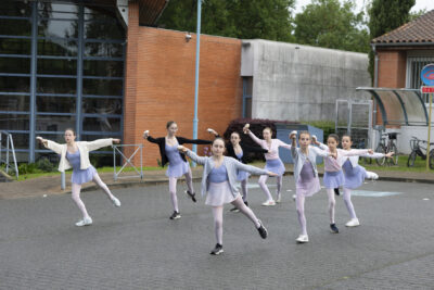 Sur le parvis de la Médiathèque de Tournefeuille, un groupe de 8 jeunes danseuses alignées écartent les bras en tutu et collant de danse, elles ont troqué les ballerines pour les chaussures de sport. - Agrandir l'image 3 sur 6, fenêtre modale