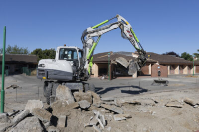 Photo d'une pelleteuse dans une cour d'école, au premier plan on voit le sol de la cour en travaux - Agrandir l'image 2 sur 2, fenêtre modale