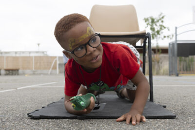 Un petit garçon à quatre pattes sur un parcours fait à partir de chaises posées en ligne, il sort de la dernière chaise - Agrandir l'image 9 sur 15, fenêtre modale