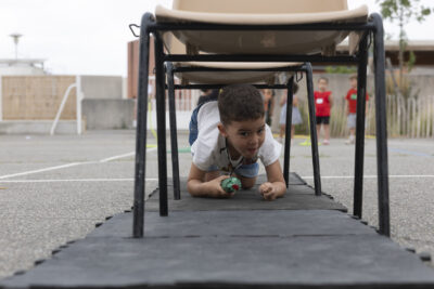 Un petit garçon à quatre pattes sur un parcours fait à partir de chaises posées en ligne - Agrandir l'image 10 sur 15, fenêtre modale