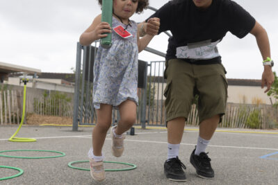 Photo d'une petite fille qui saute de cerceau en cerceau accompagnée d'un animateur - Agrandir l'image 11 sur 15, fenêtre modale