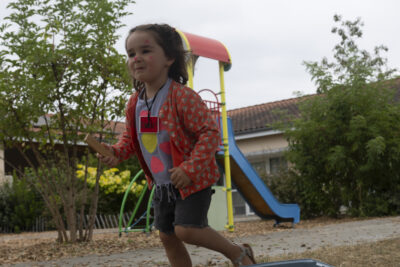 Photo d'une petite fille qui joue dans une cour, derrière elle, on voit un toboggan - Agrandir l'image 13 sur 15, fenêtre modale