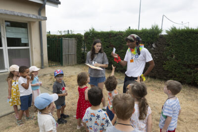 Une douzaine d'enfants rassemblés dehors, dans une cour, ils écoutent et regardent un animateur qui leur montre un papier - Agrandir l'image 14 sur 15, fenêtre modale