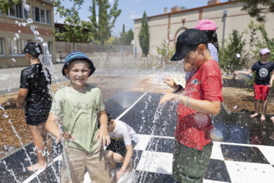 Photo de deux enfants dans des jets d'eau dans une cour d'école, d'autres enfants dans la cour jouent avec les jets d'eau - Agrandir l'image 17 sur 18, fenêtre modale