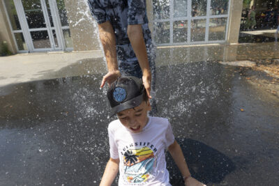 Deux jeunes garçons dans une cour d'école jouent avec un jet d'eau, un est assis dessus et l'autre debout derrière lui - Agrandir l'image 15 sur 18, fenêtre modale