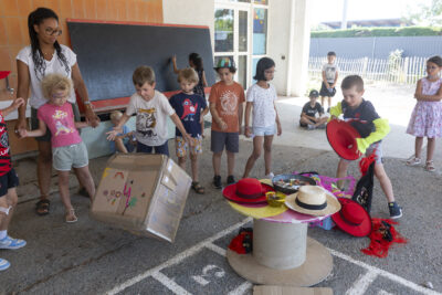 Photo d'enfants rassemblés sous un préau à l'ombre, autour d'une table ronde sur laquelle il y a des chapeaux - Agrandir l'image 6 sur 18, fenêtre modale