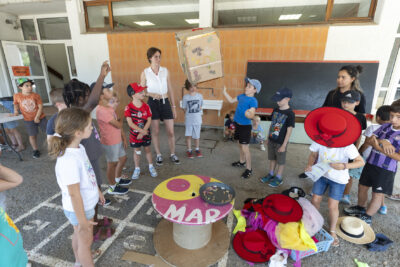 Photo d'enfants rassemblés dans une cour d'école, un enfant tient un dé géant fabriqué en carton, il y a des costumes et chapeaux de flamenco par terre - Agrandir l'image 3 sur 18, fenêtre modale
