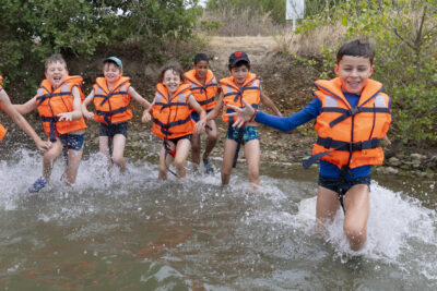 Photo d'un groupe d'enfants portant des gilets de sauvetage qui court dans l'eau - Agrandir l'image 1 sur 16, fenêtre modale