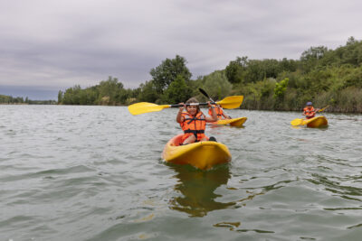 Photo d'une jeune fille sur son kayak dans le lac, qui tient les rames en l'air pour les montrer à l'objectif - Agrandir l'image 8 sur 16, fenêtre modale