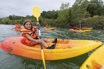 Photo d'une jeune fille qui rame sur son kayak, on voit les autres enfants derrière sur leur propre kayak - Agrandir l'image 9 sur 16, fenêtre modale