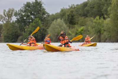 Photo de plusieurs enfants sur leurs kayaks, une jeune fille fait un signe à l'objectif - Agrandir l'image 14 sur 16, fenêtre modale