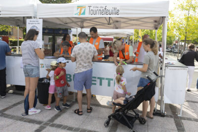 photo de la buvette avec des bénévoles en gilet orange derrière et des familles qui passent commande - Agrandir l'image 2 sur 22, fenêtre modale