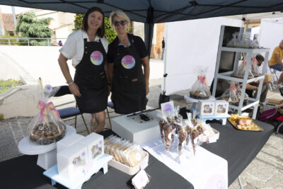 Photo d'un stand de vent de gourmandises avec deux femmes derrière le stand en tablier noir, qui sourient à l'objectif - Agrandir l'image 13 sur 22, fenêtre modale