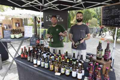 Photo d'un stand de vente de bouteilles avec deux jeunes hommes derrière le stand, tout sourire - Agrandir l'image 14 sur 22, fenêtre modale