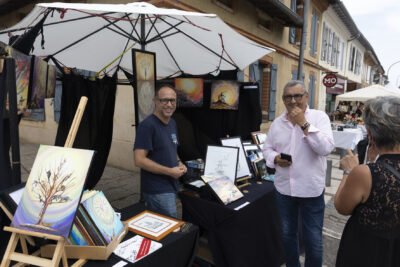 photo paysage d'un artiste qui expose ses oeuvres, le Maire est devant le stand, tous deux sourient - Agrandir l'image 16 sur 22, fenêtre modale
