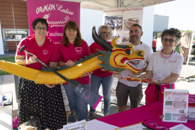 photo du stand associatif des dragon ladies, quatre femmes et un homme en ligne derrière le stand portent un dragon jaune devant eux et sourient à l'objectif - Agrandir l'image 7 sur 68, fenêtre modale