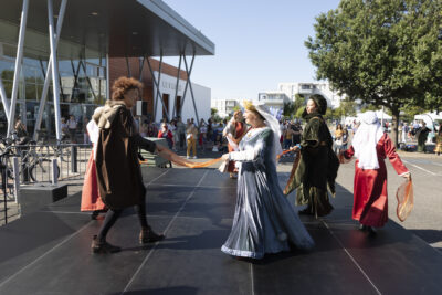 Photo d'une démonstration de danse ancienne sur la scène à l'extérieur du Phare, cinq personnes en costumes d'époque dansent, on voit des familles regarder à l'arrière-plan - Agrandir l'image 11 sur 68, fenêtre modale