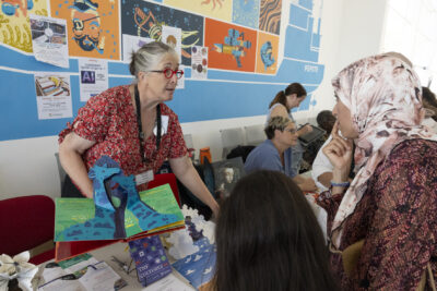 Photo d'un stand à l'intérieur, dans un couloir, une femme montre un livre pour enfants pop up avec des girafes, à une femme intéressée - Agrandir l'image 12 sur 68, fenêtre modale