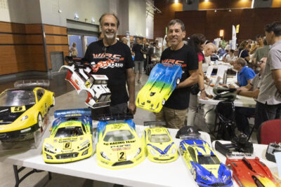 photo du stand de "wrc", deux hommes tiennent des mini véhicules en main, sur la table on voit 6 autres véhicules miniatures (la taille de la largeur de la table) - Agrandir l'image 16 sur 68, fenêtre modale
