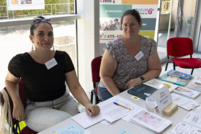 photo du stand de l'espace parentalité, deux femmes sont assises derrière, derrière elles, de grandes fenêtres qui donnent sur l'extérieur - Agrandir l'image 22 sur 68, fenêtre modale