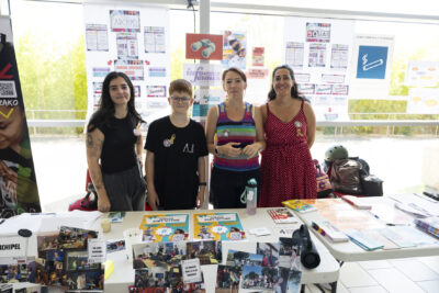 photo du stand de l'archipel, quatre jeunes derrières sourient à l'objectif, sur la table des affiches et des patchworkds de photos - Agrandir l'image 23 sur 68, fenêtre modale