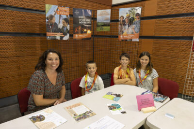 photo d'une famille à un stand, une femme et trois enfants assis, au stand éclaireurs de France, ils sourient à l'objectif - Agrandir l'image 28 sur 68, fenêtre modale