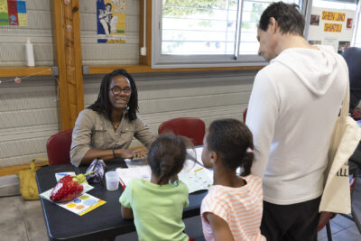 photo d'un stand derrière lequel une femme est assise et explique à une famille quelque chose - Agrandir l'image 39 sur 68, fenêtre modale