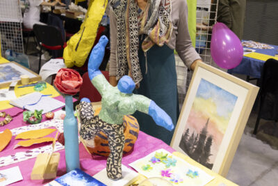 photo d'un stand de loisirs créatifs avec une femme qui sourit à l'objectif, des peintures et sculptures de papier sont sur la table - Agrandir l'image 40 sur 68, fenêtre modale
