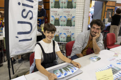 photo du stand de l'usine, une jeune femme et un jeune homme assis sourient à l'objectif, des affiches et dépliants sont sur la table - Agrandir l'image 41 sur 68, fenêtre modale