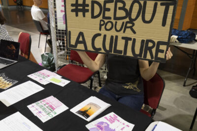photo du stand de Marionnettissimo, une femme derrière tient un carton sur lequel il est écrit "#DEBOUT POUR LA CULTURE" - Agrandir l'image 42 sur 68, fenêtre modale