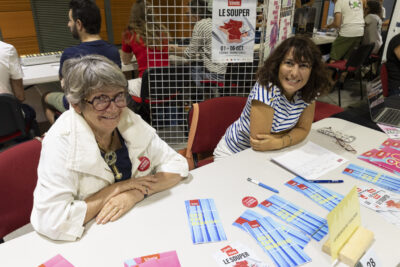 photo du stand du grenier de Toulouse, deux femmes derrière sourient à l'objectif, sur la table divers supports sont éparpillés - Agrandir l'image 43 sur 68, fenêtre modale