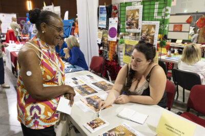 photo du stand de l'ensemble vocal de Tournefeuille, une femme montre un flyer à une autre femme qui l'écoute - Agrandir l'image 48 sur 68, fenêtre modale