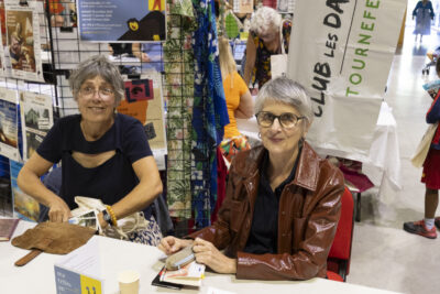 photo du stand de la compagnie OF, deux femmes assises sourient à l'objectif - Agrandir l'image 49 sur 68, fenêtre modale
