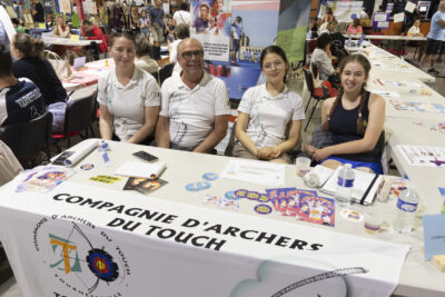 photo du stand de la compagnie des archers du touch, quatre personnes derrière le stand sourient à l'objectif - Agrandir l'image 51 sur 68, fenêtre modale
