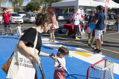 photo d'un espace hockey, avec un sol bleu, une femme et une petite fille testent en mettant le palet dans les buts avec une crosse, en extérieur ensoleillé - Agrandir l'image 6 sur 68, fenêtre modale