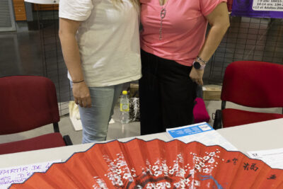 photo d'un stand avec deux femmes qui sourient à l'objectif et au premier plan un grand éventail rouge ouvert - Agrandir l'image 56 sur 68, fenêtre modale