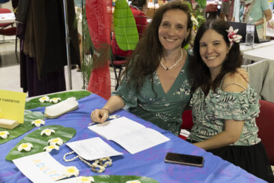 photo d'un stand de culture tahitienne, deux femmes sourient à l'objectif, sur la table sont disposées des grandes feuilles et desfleurs - Agrandir l'image 58 sur 68, fenêtre modale