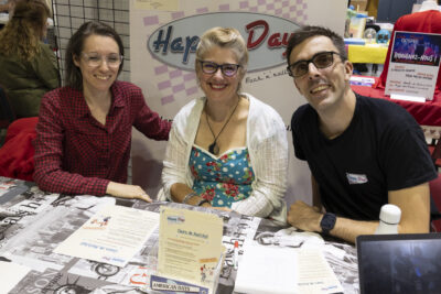 photo d'un stand de rock'n'roll, deux femmes et un homme derrière sourient à l'objectif, derrière eux, un grand panneau avec écrit "venez danser le rock'n'roll" "le bougie" - Agrandir l'image 62 sur 68, fenêtre modale