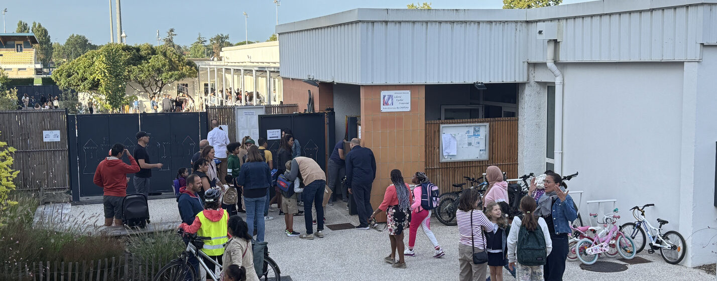 Photo de l'entrée d'une école élémentaire, des groupes de parents et enfants en train de discuter devant