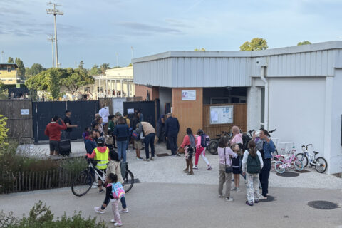 Photo de l'entrée d'une école élémentaire, des groupes de parents et enfants en train de discuter devant