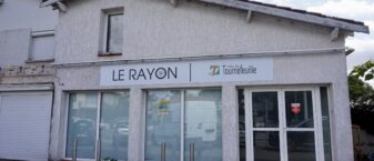 photo de la devanture du local du Rayon, on voit une façade blanche avec l'enseigne Ville de Tournefeuille Le rayon, et au rez-de-chaussée une porte vitrée et des vitres fumées