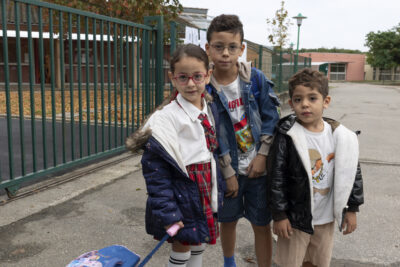 Trois enfants devant la grille d'une école regardent l'objetif - Agrandir l'image 50 sur 80, fenêtre modale