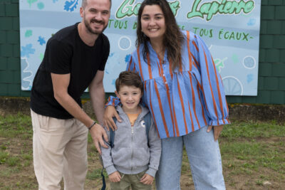 un homme, une femme et un petit garçon devant une fresque bleue avec écrit "Lapierre", le nom de l'école, sourient à l'objectif, le petit garçon entre les deux parents - Agrandir l'image 44 sur 80, fenêtre modale